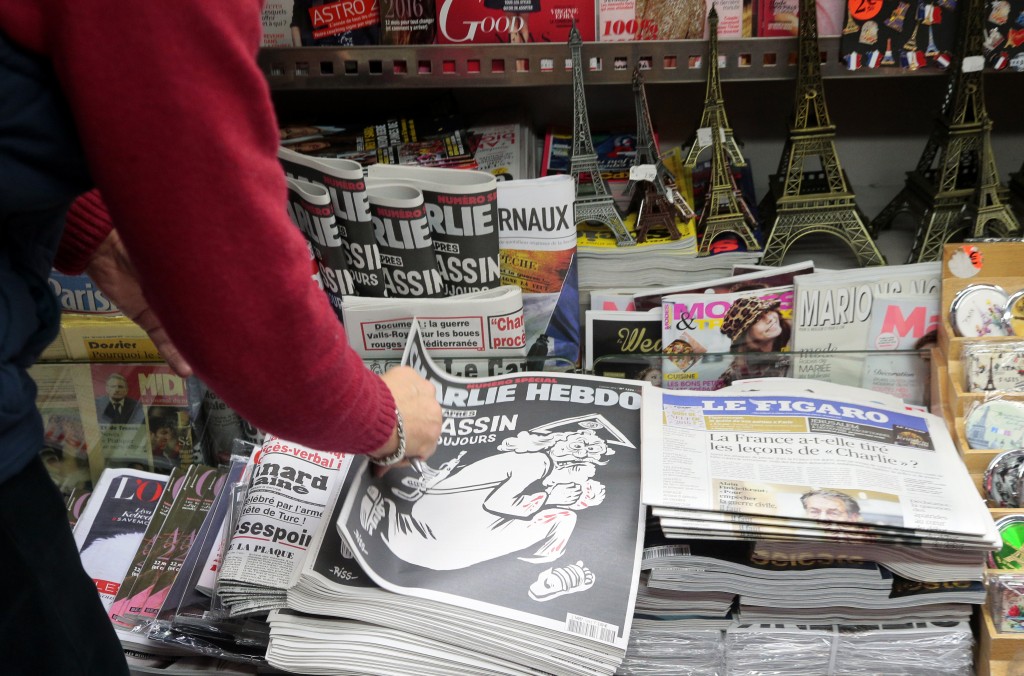 A woman looks at the special commemorative edition of French satirical newspaper Charlie Hebdo at a newsstand in Paris, on January 6, 2015, to mark the one-year anniversary of the jihadist attack that claimed the lives of 12 people, including three of its best-known cartoonists. True to form, the cover is unabashedly provocative, featuring a Kalashnikov-toting God figure wearing a blood-stained white robe, under the headline: "One year on: The killer is still at large." / AFP / JACQUES DEMARTHON