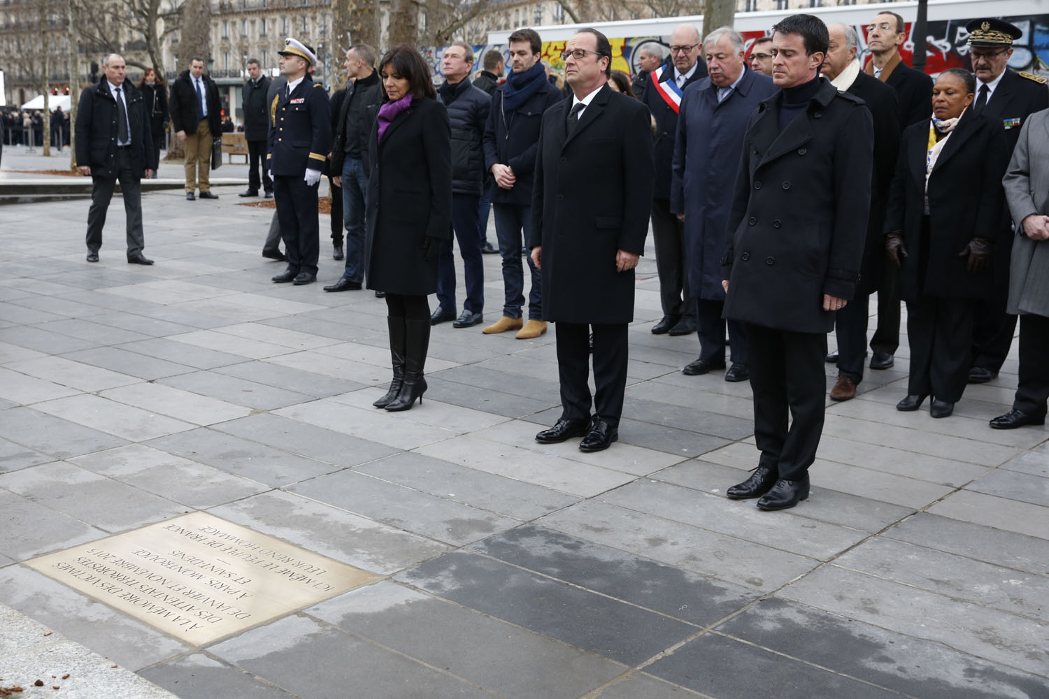 French President Francois Hollande (C), Prime Minister Manuel Valls (R) and Paris Mayor Anne Hidalgo (L) pay respect after unveiling a commemorative plaque during a ceremony held, on January 10, 2016 to mark a year since 1.6 million people thronged the French capital in a show of unity after attacks on the Charlie Hebdo newspaper and a Jewish supermarket. Just as it was last year, the vast Place de la Republique will be the focus of the gathering as people reiterate their support for freedom of expression and remember the other victims of what would become a year of jihadist outrages in France, culminating in the November 13 coordinated shootings and suicide bombings that killed 130 people and were claimed by the Islamic State (IS) group. / AFP / POOL / PHILIPPE WOJAZER