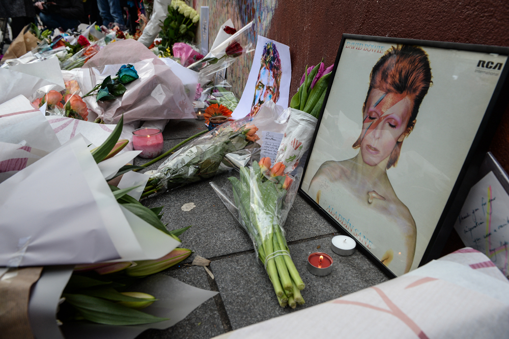 Tributes are seen beneath a mural of British singer David Bowie, following the announcement of Bowie's death, in Brixton, south London, on January 11, 2016. British music icon David Bowie died of cancer at the age of 69, drawing an outpouring of tributes for the innovative star famed for groundbreaking hits like "Ziggy Stardust" and his theatrical shape-shifting style. AFP PHOTO / CHRIS RATCLIFFE / AFP / CHRIS RATCLIFFE