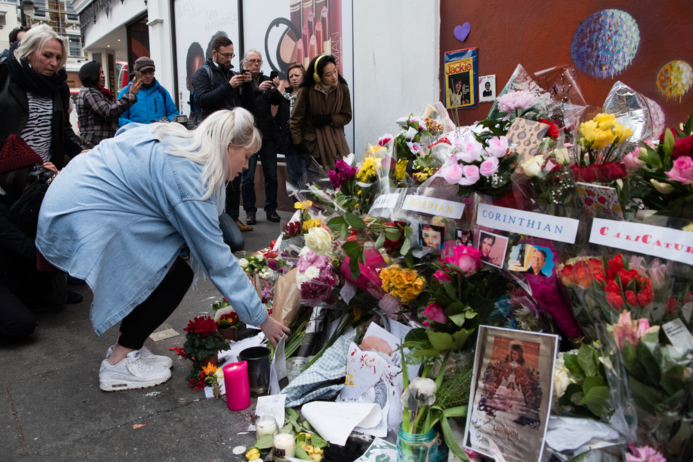 Crowds gather to read and place floral tributes beneath a mural of British singer David Bowie, in Brixton, south London, on January 12, 2016, a day after the announcement of Bowie's death. Music legend David Bowie was famously private during his lifetime -- and in death, as a string of questions about the circumstances of his passing remained unanswered. His official social media accounts had announced the shock news of his death at 69 on January 11, 2016: "David Bowie died peacefully today surrounded by his family after a courageous 18-month battle with cancer," adding a request for privacy for the grieving family. AFP PHOTO / LEON NEAL / AFP / LEON NEAL