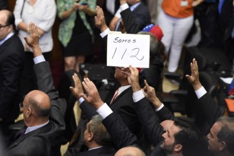 An opposition deputy raises a placard that reads "We are 112" during the new parliamentaries' swearing-in ceremony in Caracas, on January 5, 2016. Venezuela's President Nicolas Maduro ordered the security forces to ensure the swearing-in of a new opposition-dominated legislature passes off peacefully Tuesday, after calls for rallies raised fears of unrest. AFP PHOTO/JUAN BARRETO / AFP / JUAN BARRETO