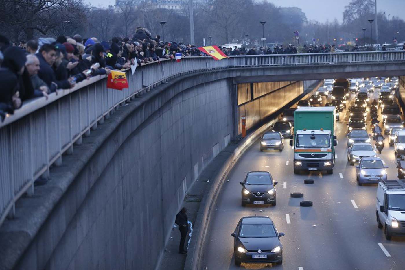 People and protestors with European countries flags stand above the ringroad (peripherique) during a taxi drivers demonstration against the VTC (transport vehicle with chauffeur) on January 26, 2016 early in the morning at porte Maillot in Paris. AFP PHOTO / THOMAS SAMSON / AFP / THOMAS SAMSON