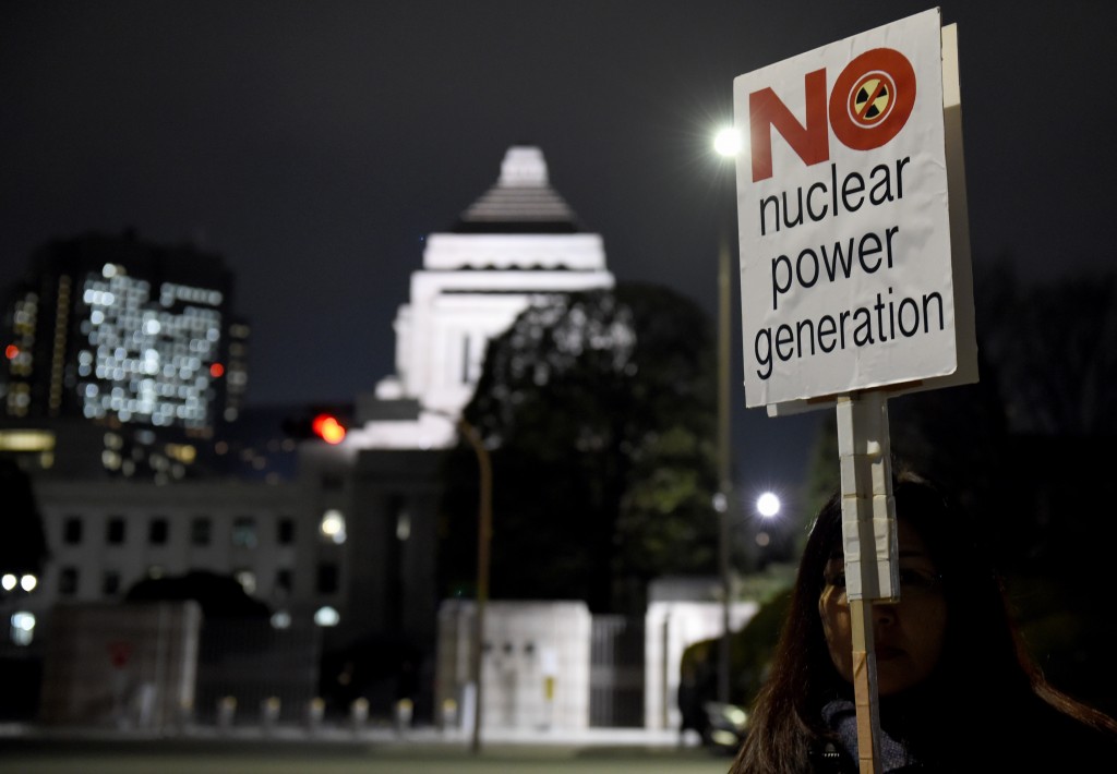 A female protester holding a placard joins an anti-nuclear demonstration rally in front of the Diet building (background) in Tokyo on March 11, 2016. Hundreds of demonstratior staged the anti-nuclear rally on the fifth anniversary day of 2011 quake and tsunami disaster in northern Japan. / AFP / TOSHIFUMI KITAMURA