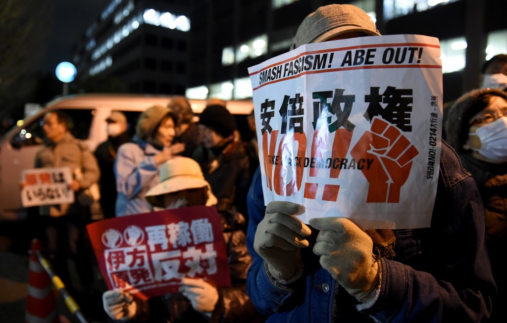 A protester (R) holds a placard saying "No, Abe administration" during an anti-nuclear demonstration rally in front of the Diet building in Tokyo on March 11, 2016. Hundreds of demonstratior staged the anti-nuclear rally on the fifth anniversary day of 2011 quake and tsunami disaster in northern Japan. / AFP / TOSHIFUMI KITAMURA