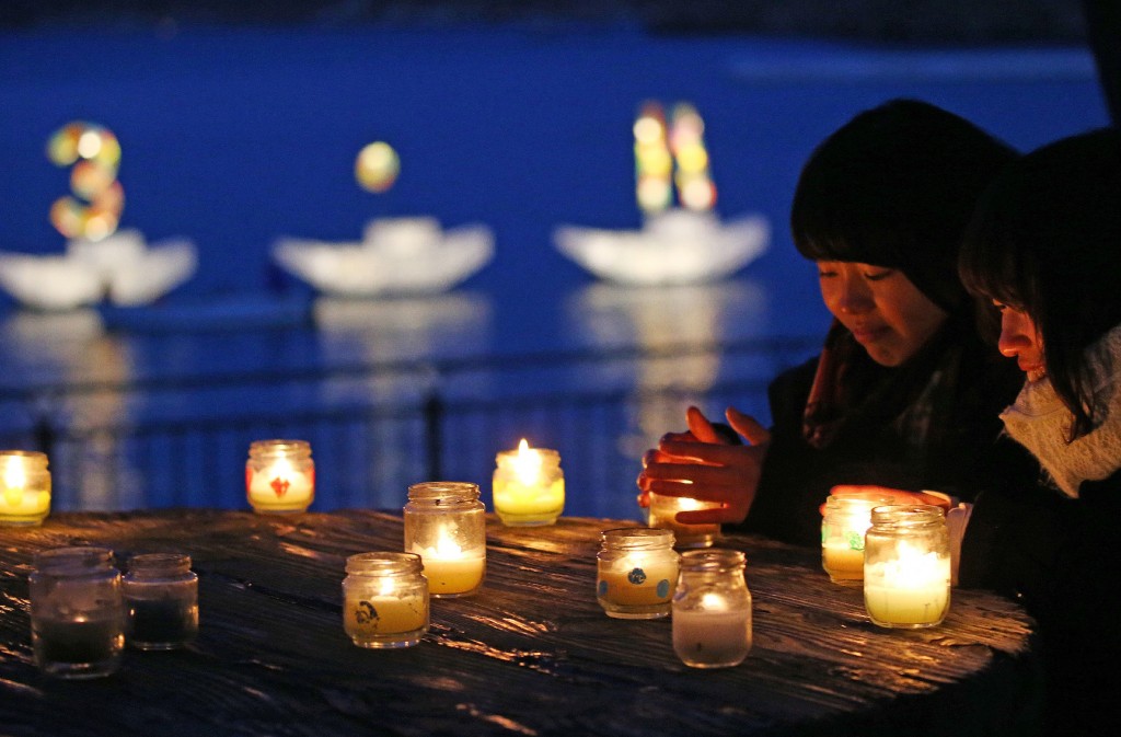 Residents pray for the quake and tsunami victims before candle lights while a candle boat displays "3.11" letters in Kamaishi, Iwate prefecture on March 11, 2016. Japan pauses on March 11 to mark five years since an offshore earthquake spawned a monster tsunami that left about 18,500 people dead or missing along its northeastern coast and sparked the worst nuclear disaster in a quarter century. / AFP / JIJI PRESS / JIJI PRESS / Japan OUT