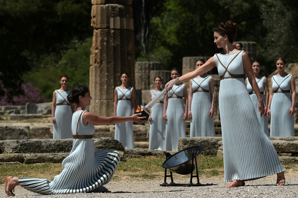 Actress Katerina Lechou (R) acting the high pristess passes the Olympic flame at the Temple of Hera on April 21, 2016 during the lighting ceremony of the Olympic flame in ancient Olympia, the sanctuary where the Olympic Games were born in 776 BC. The Olympic flame was lit Thursday in an ancient temple in one country in crisis and solemnly sent off carrying international hopes that Brazil's political paralysis will not taint the Rio Games that start in barely 100 days. / AFP PHOTO / ARIS MESSINIS