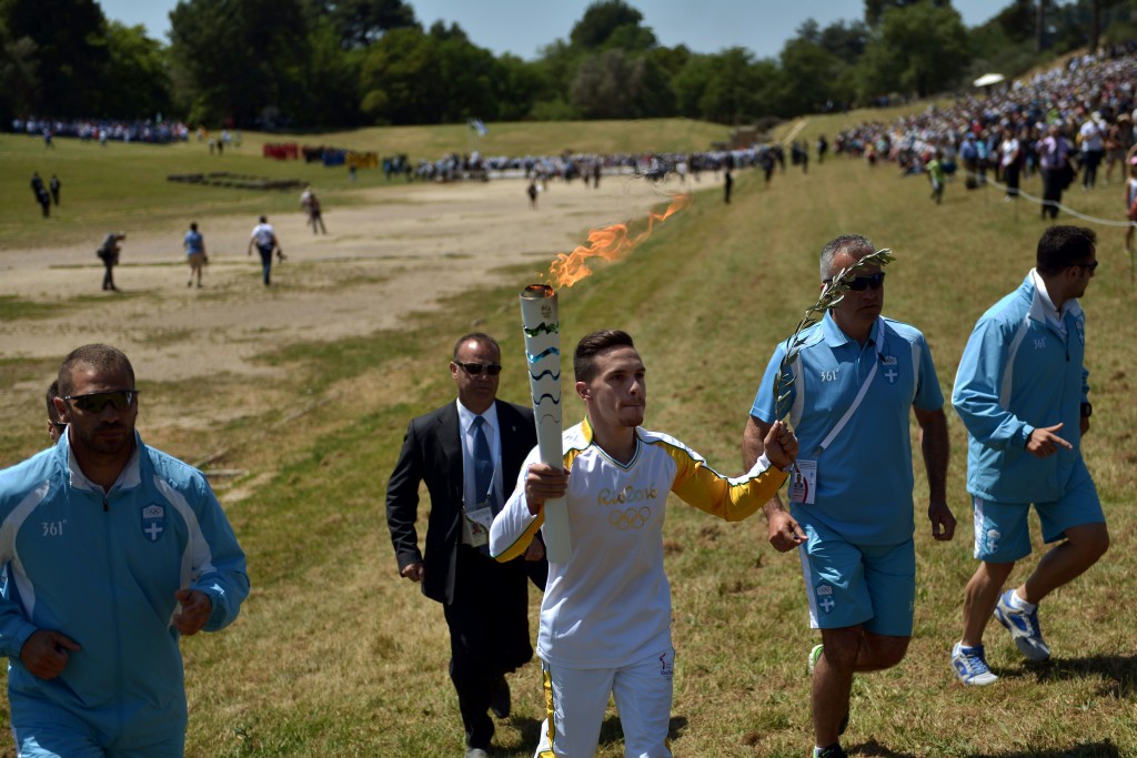 First torchbearer world champion at artistic gymnastics, Lefteris Petrounias runs with the Olympic Flame as he arrives at the Temple of Hera on April 21, 2016 during the lighting ceremony of the Olympic flame in ancient Olympia, the sanctuary where the Olympic Games were born in 776 BC. The Olympic flame was lit Thursday in an ancient temple in one country in crisis and solemnly sent off carrying international hopes that Brazil's political paralysis will not taint the Rio Games that start in barely 100 days. / AFP PHOTO / ARIS MESSINIS