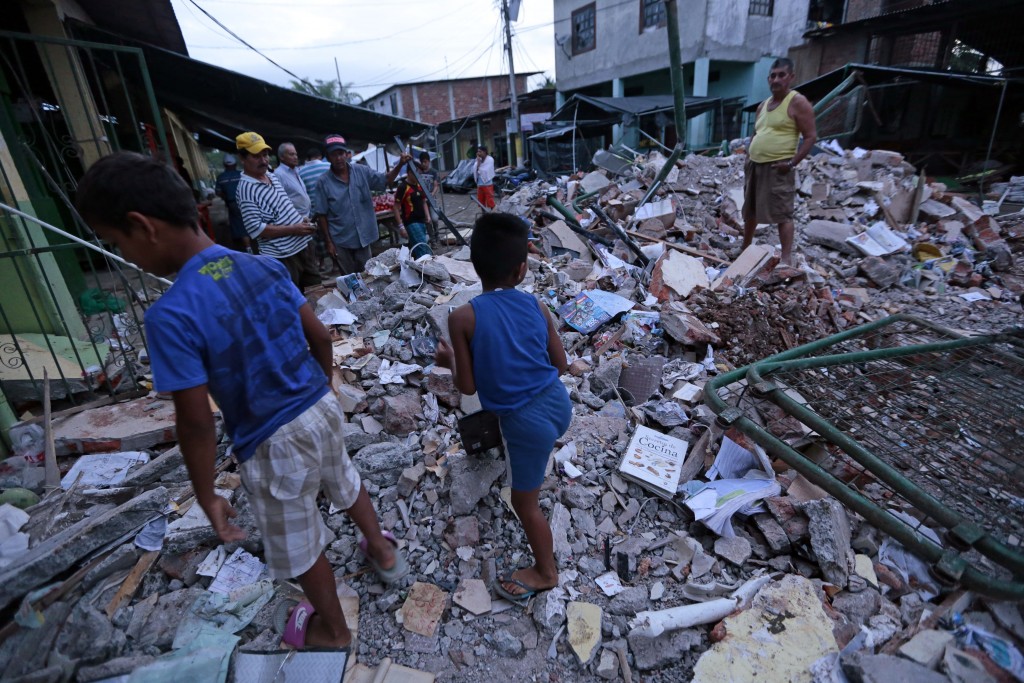 People stand amongst the rubble of fallen homes in Manta on April 17, 2016, after a powerful 7.8-magnitude earthquake struck Ecuador on April 16.  At least 77 people were killed when a powerful 7.8-magnitude earthquake struck Ecuador, destroying buildings and a bridge and sending terrified residents scrambling from their homes, authorities in the Latin American country said on April 17. / AFP PHOTO / JUAN CEVALLOS