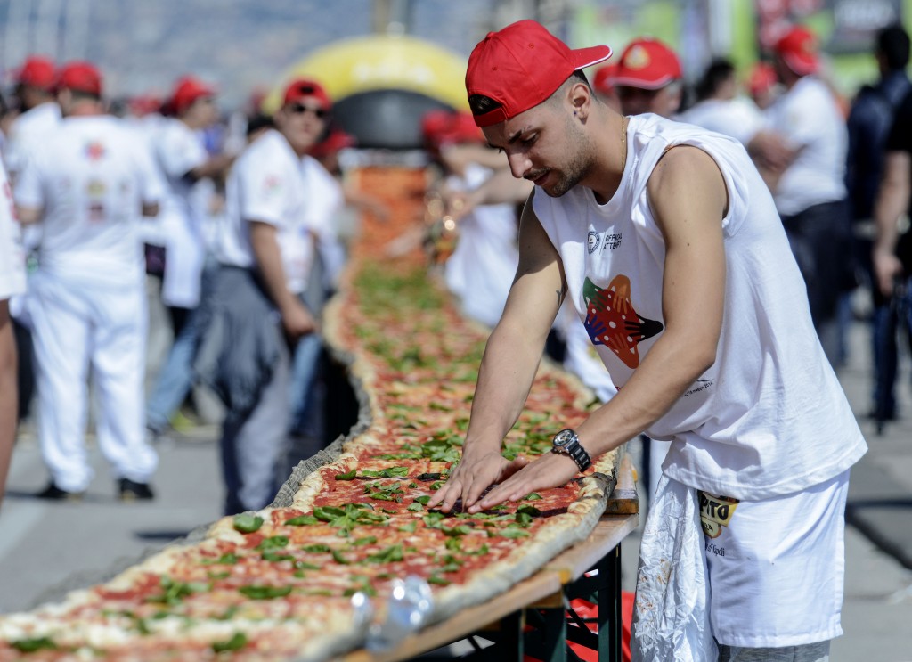 Neapolitan pizza makers attempt to make the longest pizza to break a Guinness World Record along the seafront of Naples, on May 18, 2016. For the wood-fired pizza, which measured two kilometres, they used 2,000 kg of flour, 1,600 kg of tomatoes, 2,000 kg of mozzarella, 200 litres of oil, 30kg of fresh basil. The record-breaking snack measured up at exactly 1,853.88 metres (6,082 feet), smashing the previous record of 1,595.45 metres (5,234 feet) set at last year's World Expo in Milan, Italy's food and agriculture board Coldiretti said. / AFP PHOTO / Mario LAPORTA
