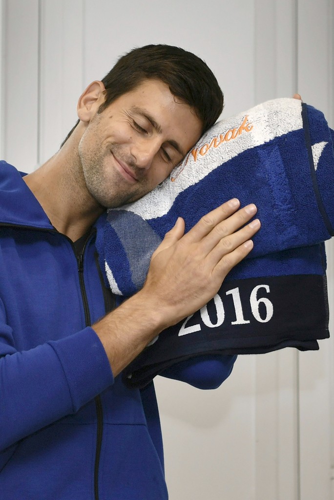 Serbia's Novak Djokovic smiles with a towel embroidered with his name after cutting his birthday cake at the Roland Garros 2016 French Tennis Open in Paris on May 22, 2016. / AFP PHOTO / Philippe LOPEZ