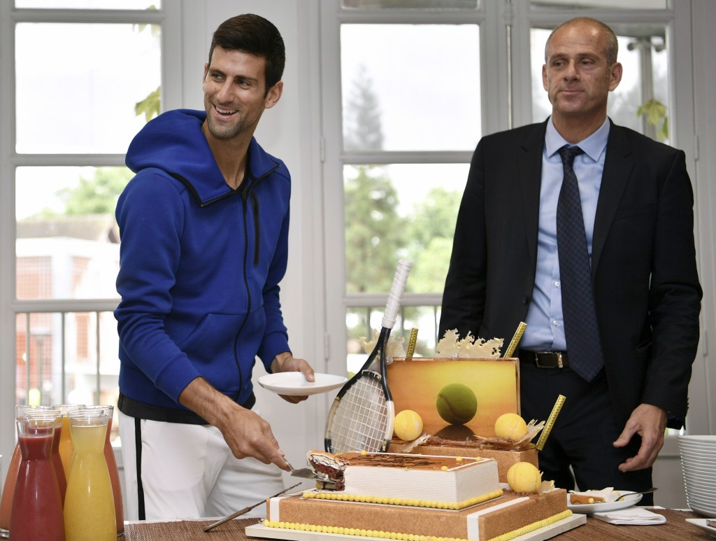 Serbia's Novak Djokovic (L) smiles next to Roland Garros Director Guy Forget as he cuts his birthday cake at the Roland Garros 2016 French Tennis Open in Paris on May 22, 2016. / AFP PHOTO / Philippe LOPEZ