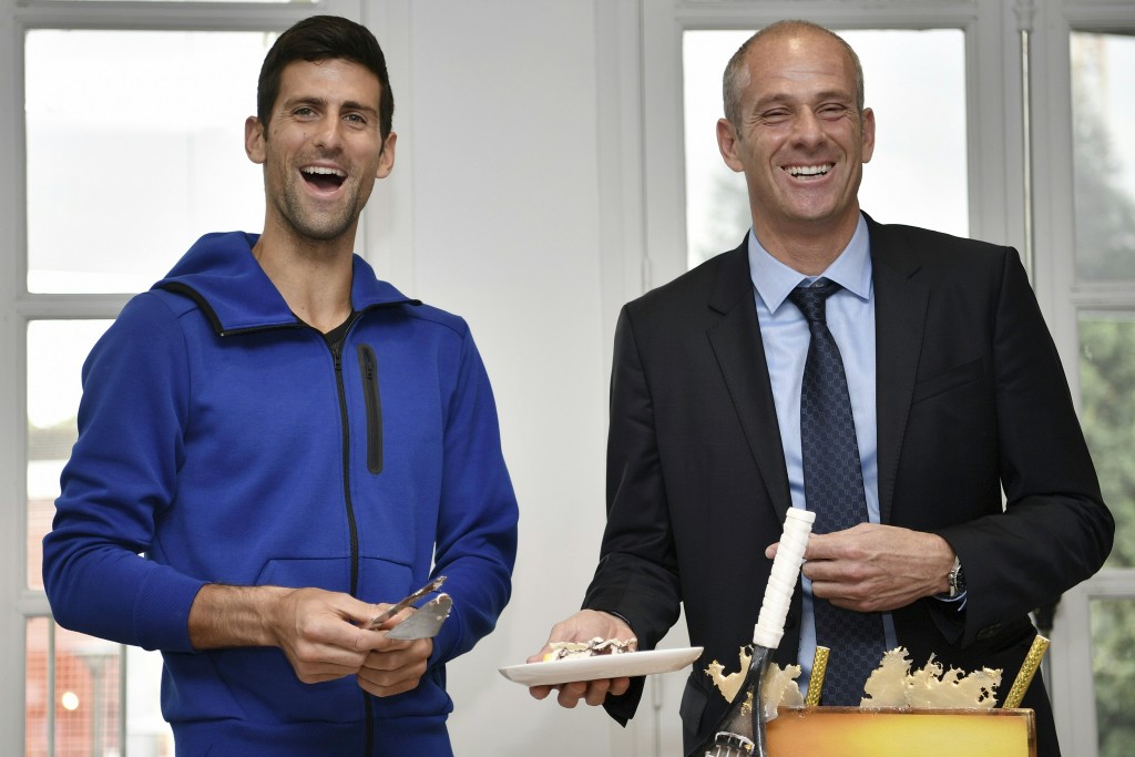 Serbia's Novak Djokovic (L) smiles next to Roland Garros Director Guy Forget as he cuts his birthday cake at the Roland Garros 2016 French Tennis Open in Paris on May 22, 2016. / AFP PHOTO / Philippe LOPEZ