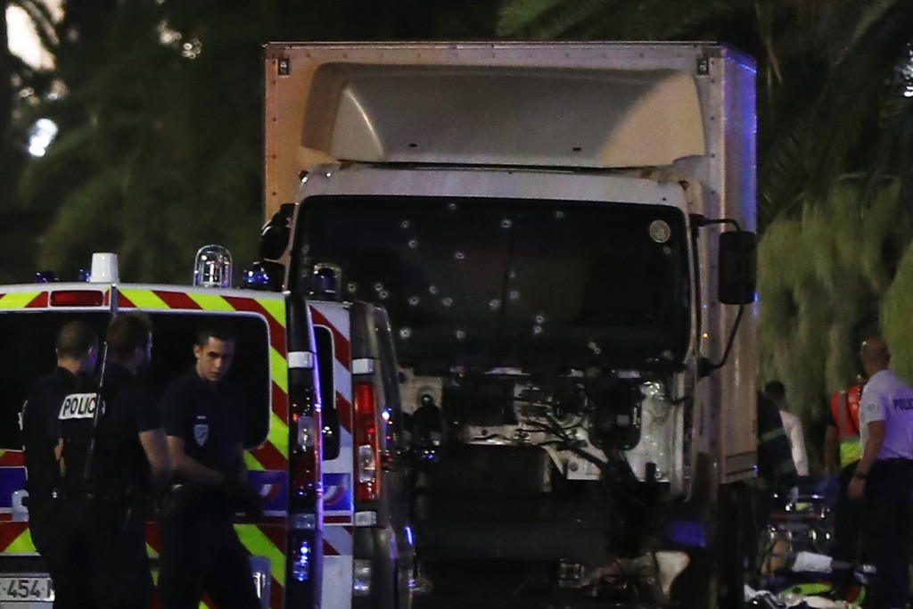 Police officers stand near a van, with its windscreen riddled with bullets, that ploughed into a crowd leaving a fireworks display in the French Riviera town of Nice on July 14, 2016. Up to 30 people are feared dead and over 100 others were injured after a van drove into a crowd watching Bastille Day fireworks in the French resort of Nice on July 14, a local official told French television, describing it as a "major criminal attack". / AFP PHOTO / VALERY HACHE