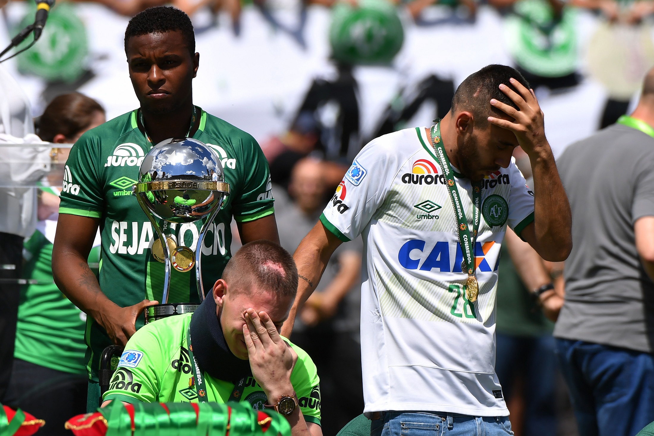 Brazilian Chapecoense footballers Alan Ruschel (R) and Jackson Follmann (C), survivors of the LaMia airplane crash in Colombia, receive the Copa Sudamericana trophy at the Arena Conda stadium in Chapeco, Santa Catarina state, in southern Brazil on January 21, 2017, before a friendly match against Palmeiras - Brazilian Champion 2016.  Most of the members of the Chapocoense football team perished in a November 28, 2016 plane crash in Colombia. / AFP PHOTO / NELSON ALMEIDA