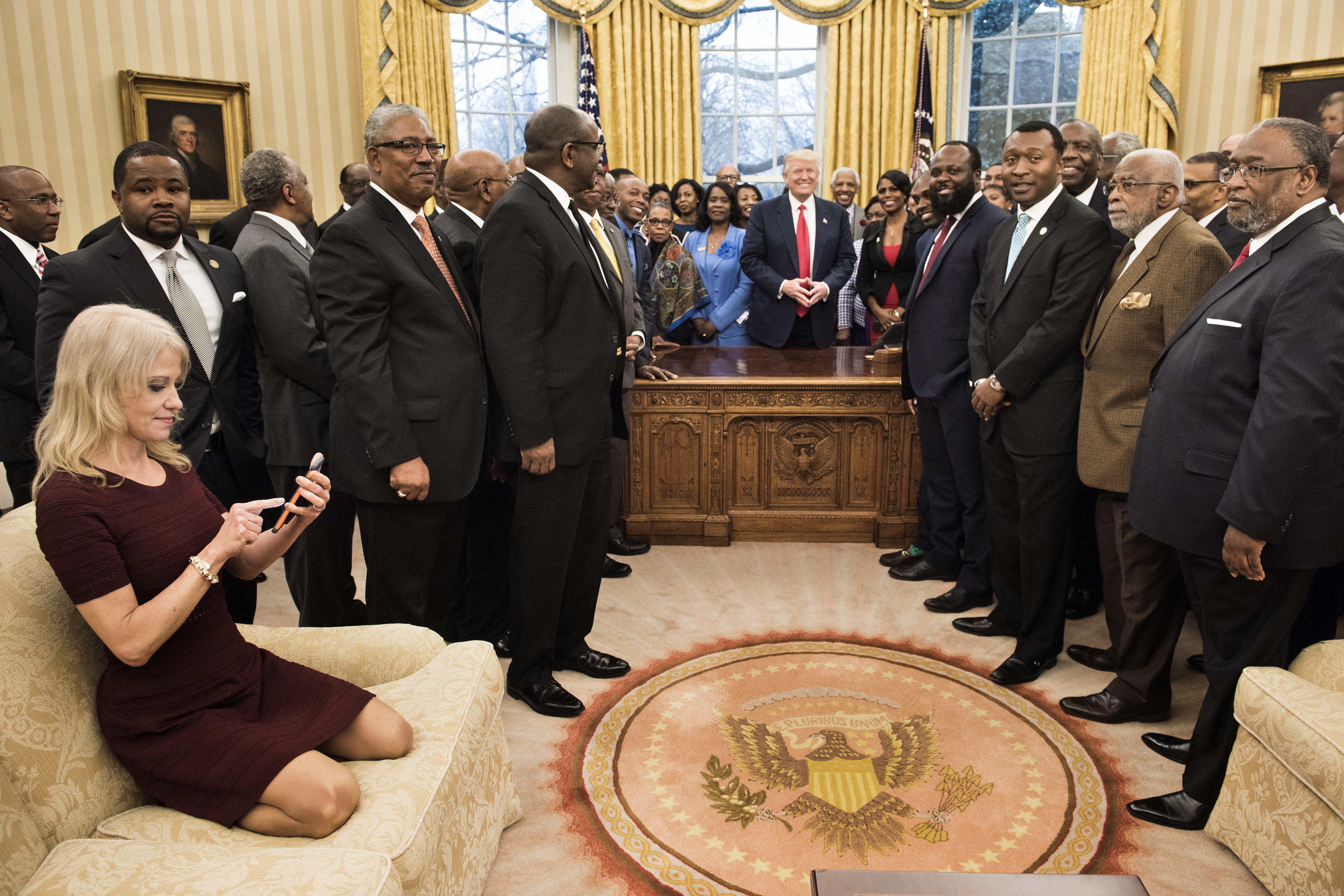 Counselor to the President Kellyanne Conway (L) checks her phone after taking a photo as US President Donald Trump and leaders of historically black universities and colleges pose for a group photo in the Oval Office of the White House before a meeting with US Vice President Mike Pence February 27, 2017 in Washington, DC. / AFP PHOTO / Brendan Smialowski